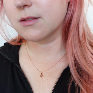 May include: A close-up of a person wearing a black shirt and a delicate gold necklace with a small heart pendant.