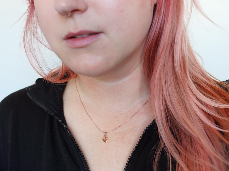 May include: A close-up of a person wearing a black shirt and a delicate gold necklace with a small heart pendant.