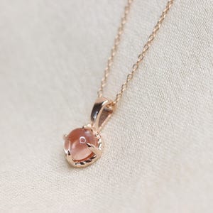 May include: A delicate rose gold necklace with a round, light pink gemstone pendant.