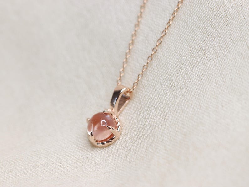 May include: A delicate rose gold necklace with a round, light pink gemstone pendant.