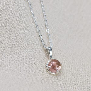May include: A silver chain necklace with a pink gemstone pendant. The pendant is set in a silver bezel.