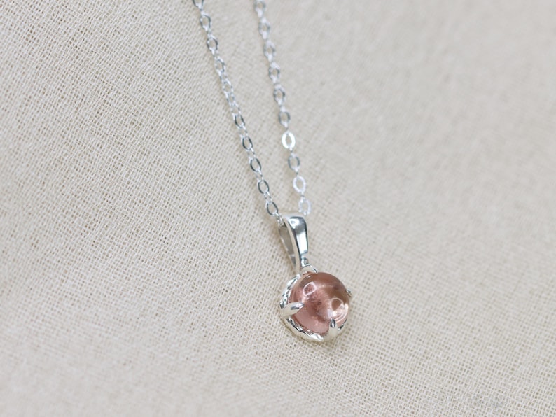 May include: A silver chain necklace with a pink gemstone pendant. The pendant is set in a silver bezel.