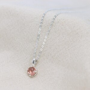 May include: A delicate silver chain necklace with a small, round, light pink gemstone pendant.