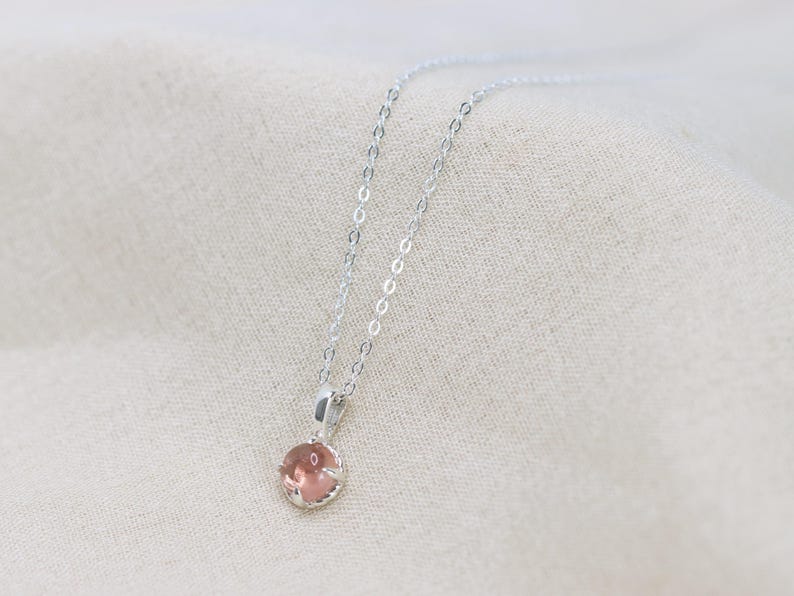 May include: A delicate silver chain necklace with a small, round, light pink gemstone pendant.