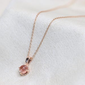 May include: A delicate rose gold necklace with a small, round, light pink gemstone pendant.