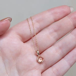 May include: A delicate gold chain necklace with a small, round, light pink gemstone pendant.