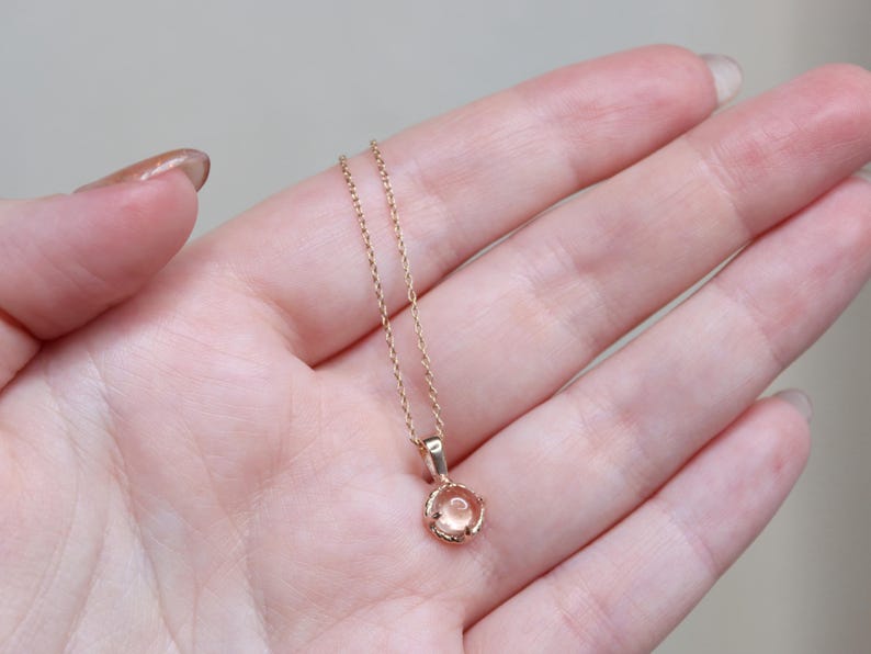 May include: A delicate gold chain necklace with a small, round, light pink gemstone pendant.