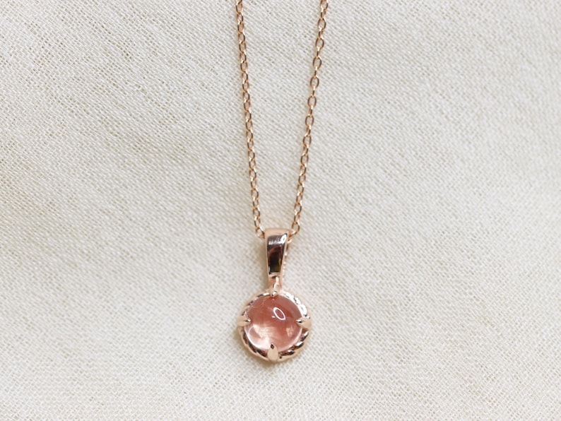 May include: A delicate rose gold necklace with a small, round, light pink gemstone pendant.