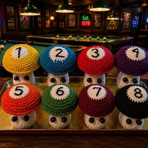 May include: Eight crocheted mushroom-shaped figures arranged on a metal tray. Each mushroom cap features a different color—yellow, blue, red, purple, orange, green, maroon, and black—with a white circular center displaying a black number from 1 to 8.