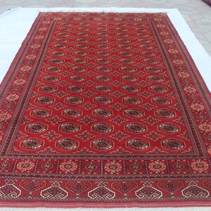 May include: A rectangular red rug with an intricate pattern of repeating oval and floral designs. The rug has a detailed border with geometric and floral motifs. The rug is displayed on a white surface.