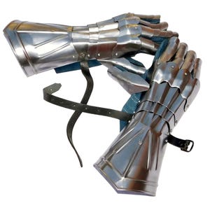 May include: A pair of articulated steel gauntlets featuring overlapping metal plates that cover the fingers, hand, and wrist. The gauntlets have a polished silver finish, blue interior lining, and black leather straps with metal buckles for secure fastening.