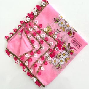 May include: A square pink headscarf featuring a floral print with white, yellow, and red flowers. The edges are finished with intricate needle lace in shades of dark green, bright pink, and white. The fabric includes the text ERIPEK Made in Türkiye.