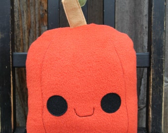 May include: A red plush apple pillow with a green stem and a smiling face. The pillow is sitting on a black wooden surface.