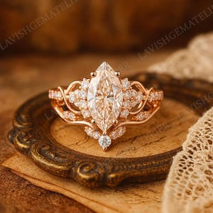 Puede incluir: Anillo de compromiso con diamante talla marquesa y banda de oro rosa. El anillo presenta un gran diamante central y diamantes de acento más pequeños. El diseño incluye filigranas intrincadas y un engaste ornamentado. Se muestra sobre un fondo de estilo vintage.