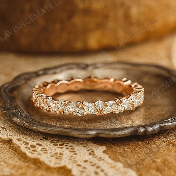 May include: Rose gold eternity ring with alternating marquise and round-cut diamonds. The ring is displayed on a decorative, antique-style plate. The ring is a piece of jewellery.