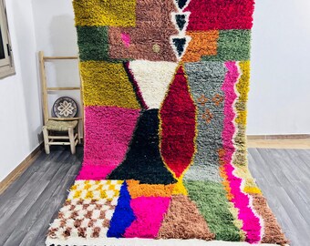 May include: A vibrant, handmade rug with a patchwork design. The rug features a mix of colors including pink, yellow, green, and red. It has a geometric pattern with a white fringe along the bottom edge. The rug is made of a soft, textured material.