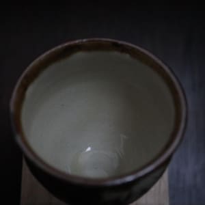 May include: A handcrafted ceramic bowl with a dark brown rim and a light interior. The bowl has a simple, elegant design, suitable for serving soups, cereals, or other dishes. The bowl is likely made of stoneware or porcelain.