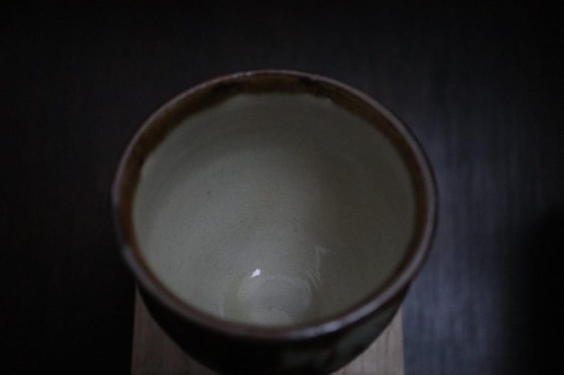 May include: A handcrafted ceramic bowl with a dark brown rim and a light interior. The bowl has a simple, elegant design, suitable for serving soups, cereals, or other dishes. The bowl is likely made of stoneware or porcelain.