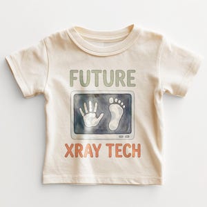 May include: Cream-colored baby t-shirt with the words "FUTURE XRAY TECH" in green and orange. The shirt features a graphic of a hand and footprint on a screen, resembling an X-ray.