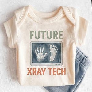 May include: Cream-colored baby onesie with the words "FUTURE XRAY TECH" in green and orange. The onesie features a graphic of a hand and foot x-ray. Light blue baby pants are visible.
