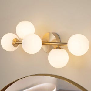 Könnte beinhalten: Moderne Wandleuchte mit fünf kugelförmigen, satinierten Glasschirmen. Die Leuchte hat eine Messingoberfläche und ist an einer neutralfarbenen Wand montiert. Das Design ist minimalistisch und eignet sich für Bad oder Schlafzimmer.