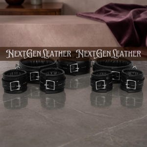 May include: Black leather restraints with silver buckles are displayed. The set includes wrist cuffs and neck restraints. The text "NEXTGEN LEATHER" is displayed across the top of the image.