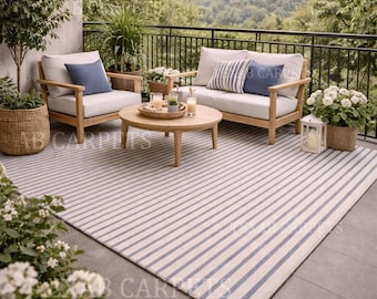 Peut inclure: Scène de patio extérieur avec un tapis rayé bleu et blanc. Le mobilier comprend des chaises et un canapé en bois avec des coussins crème et bleus. Une table basse ronde en bois et des plantes en pot sont également présentes. Un paysage urbain est visible en arrière-plan.