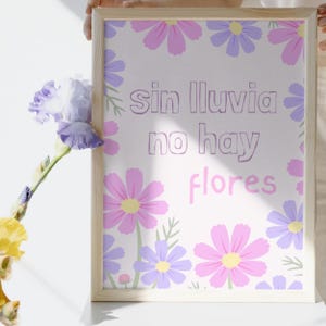 May include: A framed print with the Spanish text "sin lluvia no hay flores" (without rain, there are no flowers). The print features a white background with pink and purple flowers. The frame is light-colored wood.