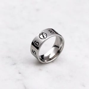 Puede incluir: Un anillo plateado con los números negros 5, 6, 7 y 8 alrededor de la banda. El anillo tiene una superficie pulida y reflectante. Los números están en una fuente clara y en negrita. El anillo es probablemente de acero inoxidable.