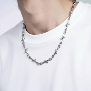 Peut inclure: Un collier argenté avec un motif de fil de fer barbelé. Le collier est porté autour du cou et est en métal. Un bijou unique.