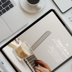 May include: A flat lay featuring a laptop, tablet, coffee cup, smartphone, and wireless earbuds on a white surface. The tablet displays text that reads "Things I do to feel aligned again."