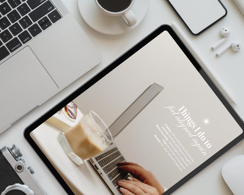 May include: A flat lay featuring a laptop, tablet, coffee cup, smartphone, and wireless earbuds on a white surface. The tablet displays text that reads "Things I do to feel aligned again."