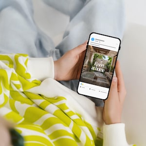 May include: A smartphone screen shows a social media post with the text "Resort at home." The phone is held by a person wearing a white and yellow patterned sweatshirt and light blue jeans. The phone screen displays an image of a luxurious outdoor space.