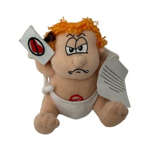 May include: A plush doll with orange hair and a grumpy facial expression, wearing a white diaper. The doll holds a white sign with a red circle and a diagonal line through a heart. A white tag with FCC compliance text is attached to the side.