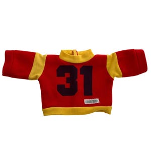 Puede incluir: Jersey rojo y amarillo de estilo vintage con el número 31 en negro. El jersey tiene mangas y cuello amarillos, con cremallera en el cuello. Una pequeña etiqueta es visible en la parte inferior.