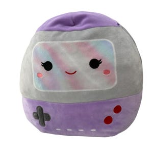 May include: A plush, round, purple and gray toy resembling a retro handheld game console. The screen displays a pastel rainbow design with a smiling face, black eyes, and pink cheeks. The bottom has a directional pad and red buttons.