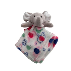 May include: A baby comforter with a grey elephant head and a patterned blanket. The blanket has a white background with pink, blue, and green designs. The elephant has large ears and a trunk.