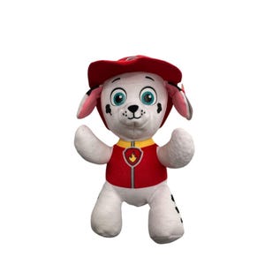 May include: A plush toy of Marshall from Paw Patrol. The white dog has a red firefighter hat and vest with a yellow collar. The toy has black spots, blue eyes, and is standing with its arms up.
