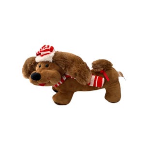 Puede incluir: Un perro de peluche marrón con un gorro y bufanda de Papá Noel a rayas rojas y blancas. El perro tiene una nariz negra y una boca roja. El perro está tumbado y tiene una silla de montar a rayas rojas y blancas.