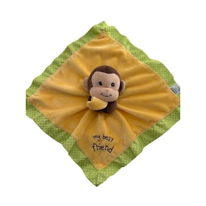 May include: A yellow baby blanket with a plush monkey toy attached. The blanket has a green polka dot border and the words "my best friend" are embroidered on the corner. The monkey is brown and tan.
