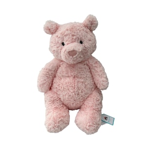 May include: A plush pink teddy bear with a textured, fuzzy exterior. The bear has small black eyes, a rounded nose, and small, rounded ears. The bear is standing upright and has a tag attached to its side.