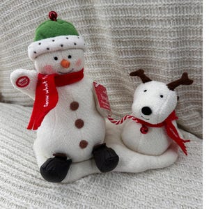 Könnte beinhalten: Weihnachtsdekoration mit einem Schneemann und einem Rentier. Der Schneemann hat einen grünen Hut und einen roten Schal, das Rentier hat braunes Geweih und einen roten Schal. Beide sind weiß und sitzen auf einer weißen Basis.