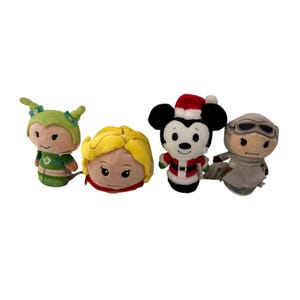 Op de afbeelding: Vier pluche karakter speelgoed. Eén is groen met een groene hoed, één heeft blond haar en een rode sjaal, één is Mickey Mouse in een kerstmanpak en de laatste is een grijs karakter met een bril. Allemaal op een witte achtergrond.