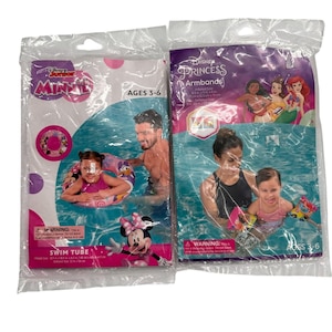 May include: Two plastic packages containing Disney swimming accessories. The left package features a pink Minnie Mouse swim tube for ages 3-6. The right package contains Disney Princess armbands for ages 3-6, with printed dimensions of 22 cm x 13 cm x 15 cm.