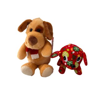 May include: Two plush dog toys. One is tan with brown ears and a red and white scarf. The other is red with a festive pattern of green, white, and yellow circles and snowflakes. Both are sitting upright.