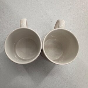 Puede incluir: Dos tazas de cer&aacute;mica blanquecina con asas curvas se colocan una al lado de la otra. Las tazas tienen un dise&ntilde;o sencillo y cl&aacute;sico, con un acabado liso y brillante. El interior de cada taza es de un tono ligeramente m&aacute;s oscuro de blanquecino.