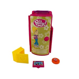 May include: A Polly Pocket playset featuring a pink and green case with a Polly Pocket graphic. Includes a yellow book-shaped accessory, a small pink screen, and an orange circular piece. The case has a button and a flower pattern.