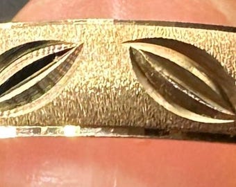 May include: A gold-colored ring with a textured surface and engraved leaf-shaped designs. The ring has a polished, shiny edge. The ring is a jewelry item.