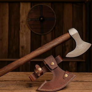 May include: A traditional axe with a wooden shaft and a silver blade, displayed on a wooden surface. The blade has an etched pattern. A brown leather sheath with brass studs protects the axe head. The background features a wooden shield and wall.