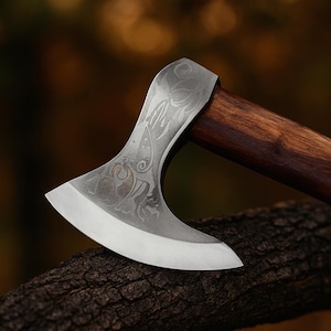 May include: A detailed view of a silver axe head with ornate engravings and a dark wooden handle. The axe blade is curved and sharp. The handle is a deep brown colour. The axe rests on a piece of wood.